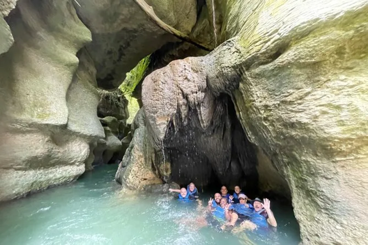 Group of people in a rocky cave with water, smiling and waving.