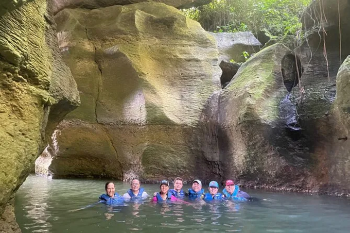 Group of seven people in a rocky cave pool, wearing life jackets.