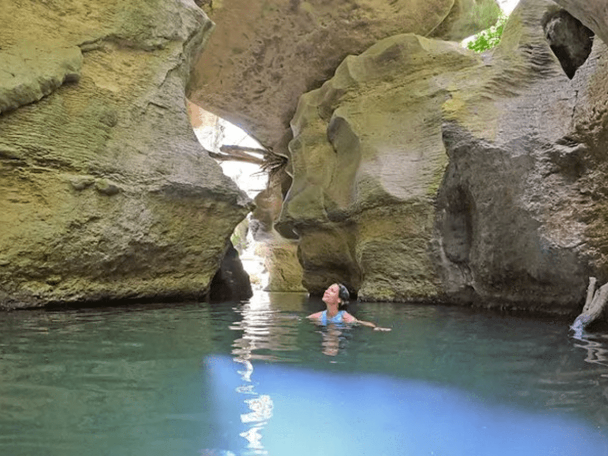 Person swimming in a clear pool surrounded by large rock formations.