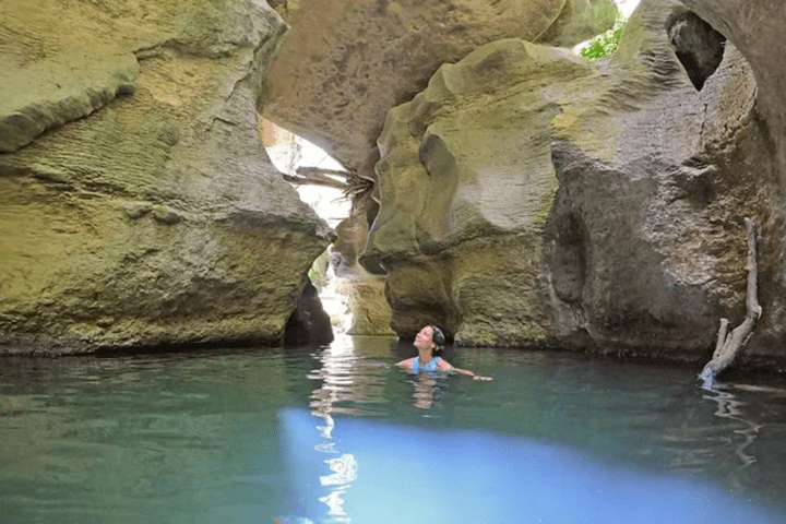 Person swimming in a clear pool surrounded by large rock formations.