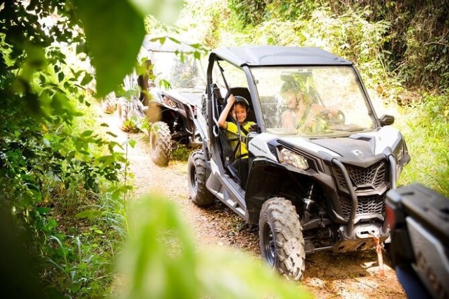 Two off-road vehicles driving on a dirt path with a child smiling in the front car.