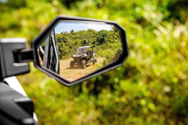 Off-road vehicle reflected in side mirror with green foliage background.