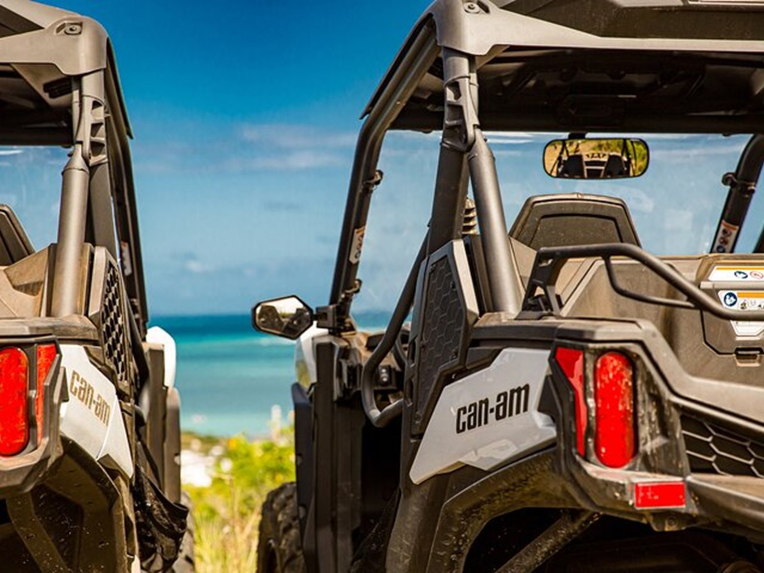Two off-road vehicles parked with a view of the ocean and blue sky in the background.