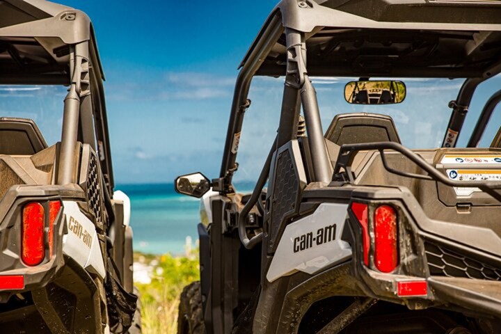 Two off-road vehicles parked with a view of the ocean and blue sky in the background.