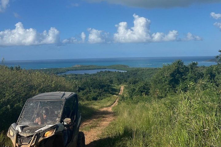 ATV on dirt path with ocean view, under a bright blue sky and fluffy clouds.