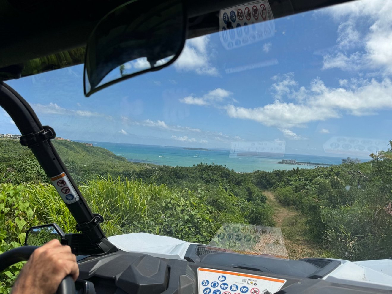 View from inside a vehicle driving downhill with ocean and sky visible in the background.
