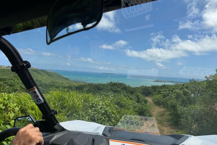 View from inside a vehicle driving downhill with ocean and sky visible in the background.
