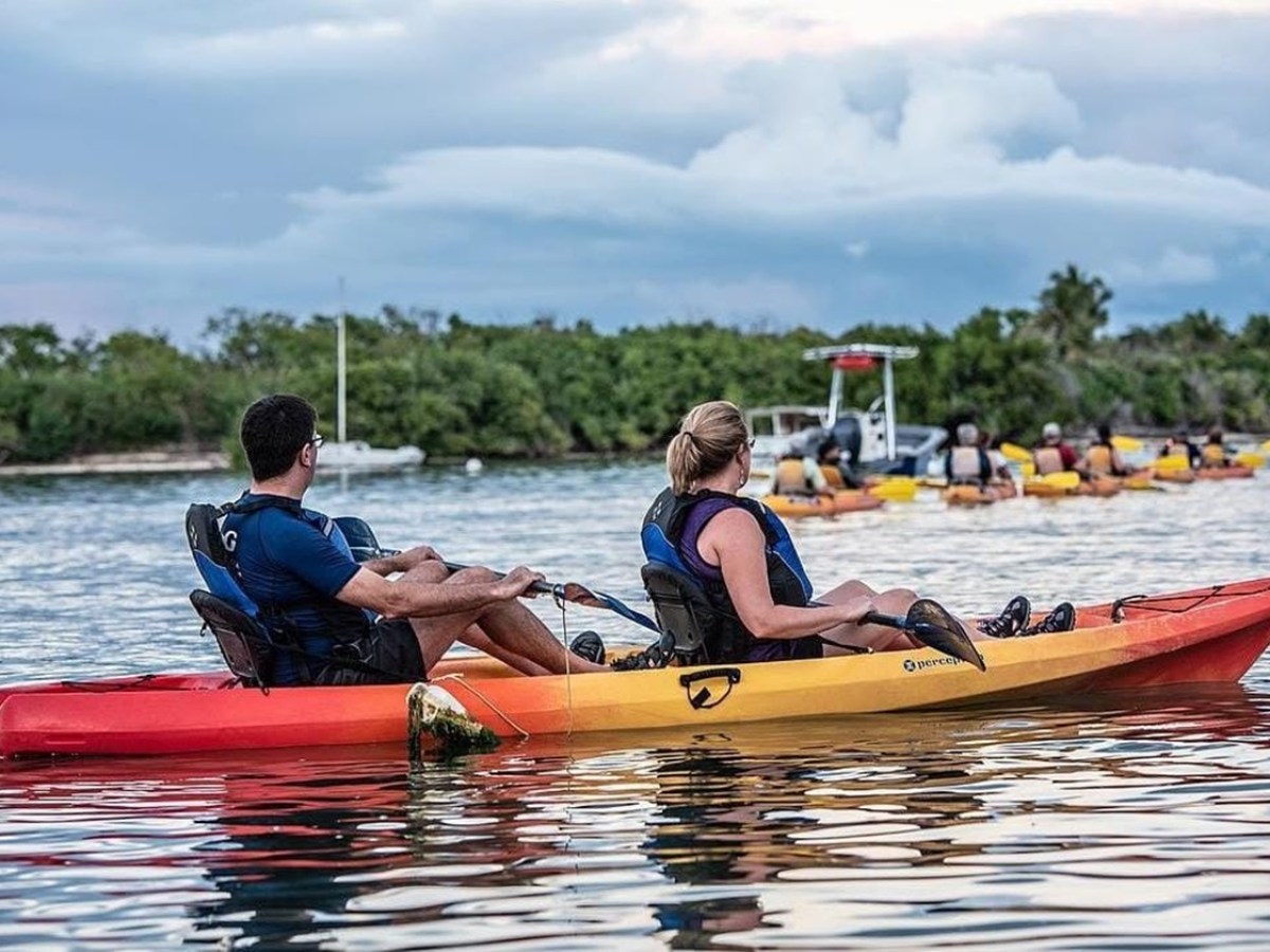 Two people in a tandem kayak on a calm river with others in the distance.