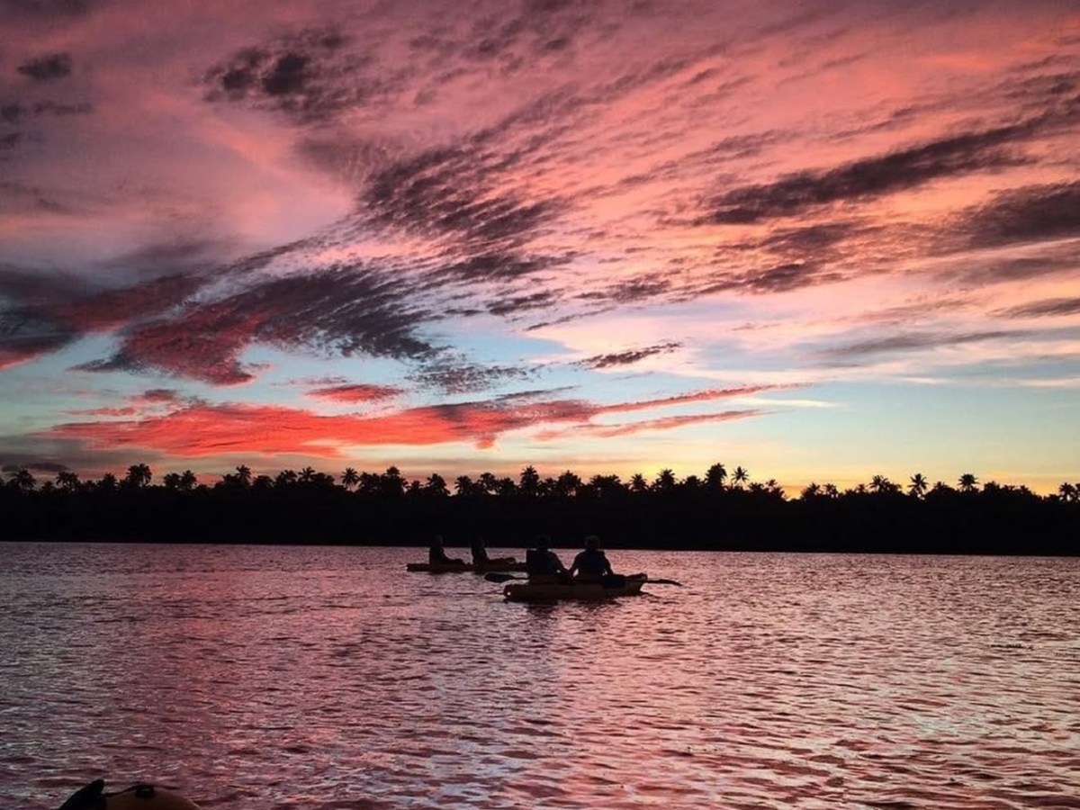 Kayakers on a calm water at sunset with vibrant pink and purple clouds in the sky.