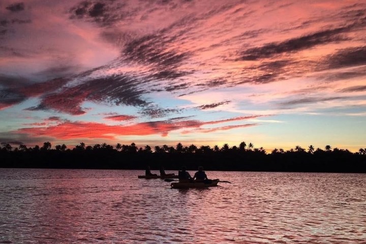 Kayakers on a calm water at sunset with vibrant pink and purple clouds in the sky.