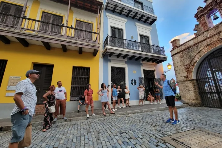 Group of people on a cobblestone street beside a blue building with balconies.