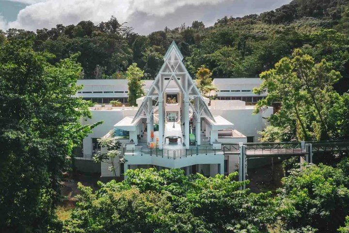 Modern white building with triangular roof surrounded by lush green trees.