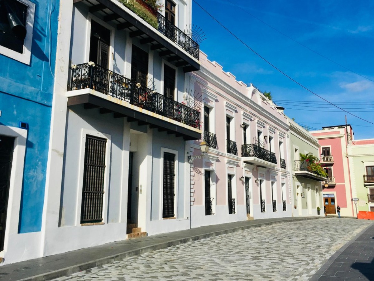 Colorful buildings with balconies line a cobblestone street under a blue sky.