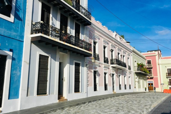 Colorful buildings with balconies line a cobblestone street under a blue sky.