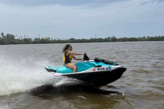 Person riding a teal jet ski on a lake with trees in the background.