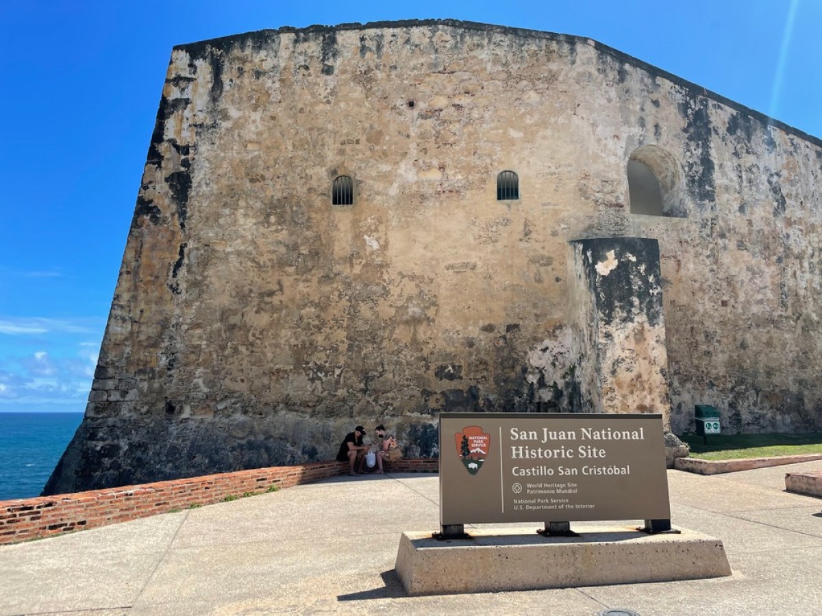 Old stone fort wall with sign reading 'San Juan National Historic Site Castillo San Cristóbal'.