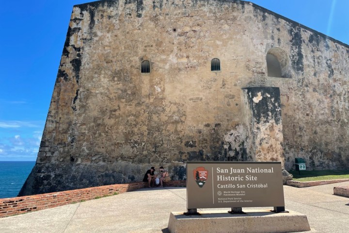 Old stone fort wall with sign reading 'San Juan National Historic Site Castillo San Cristóbal'.