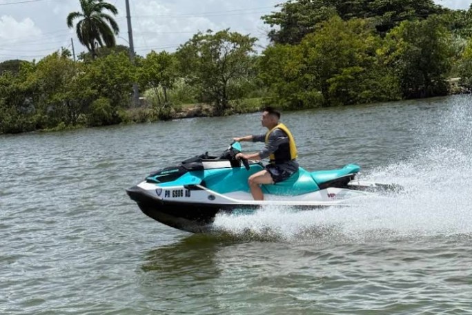Person riding a jet ski on a lake with trees in the background.