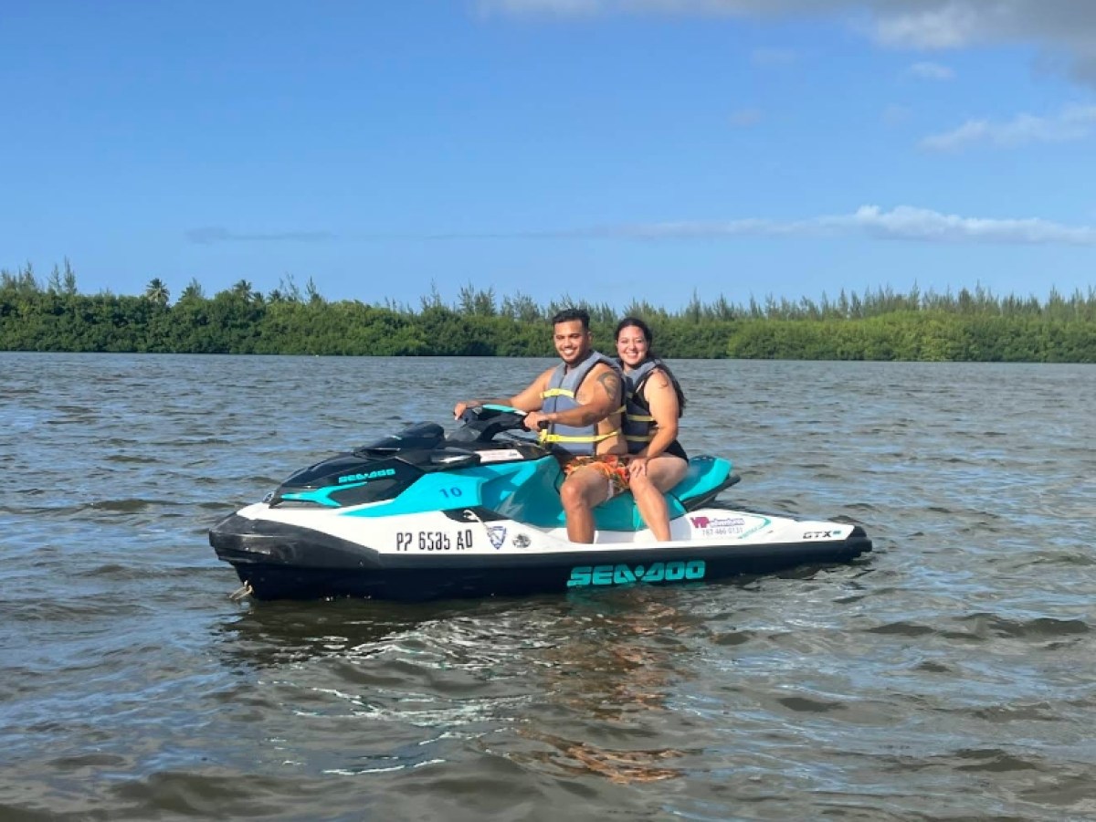 Two people on a jet ski in a calm body of water with trees in the background.