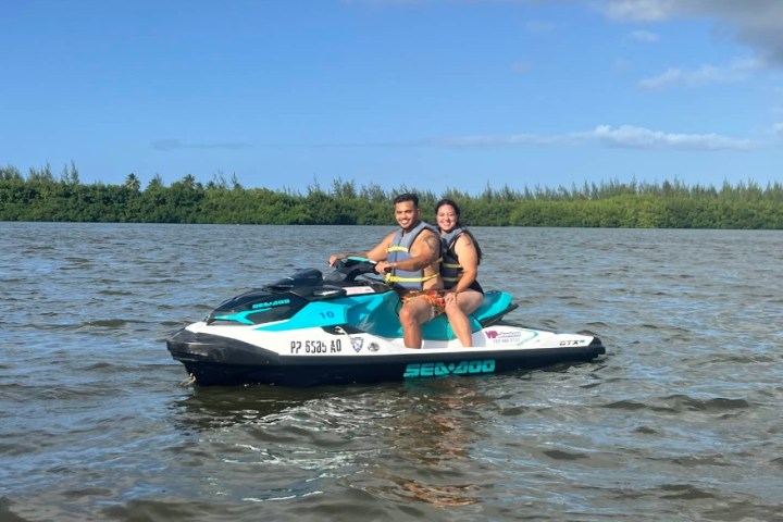 Two people on a jet ski in a calm body of water with trees in the background.