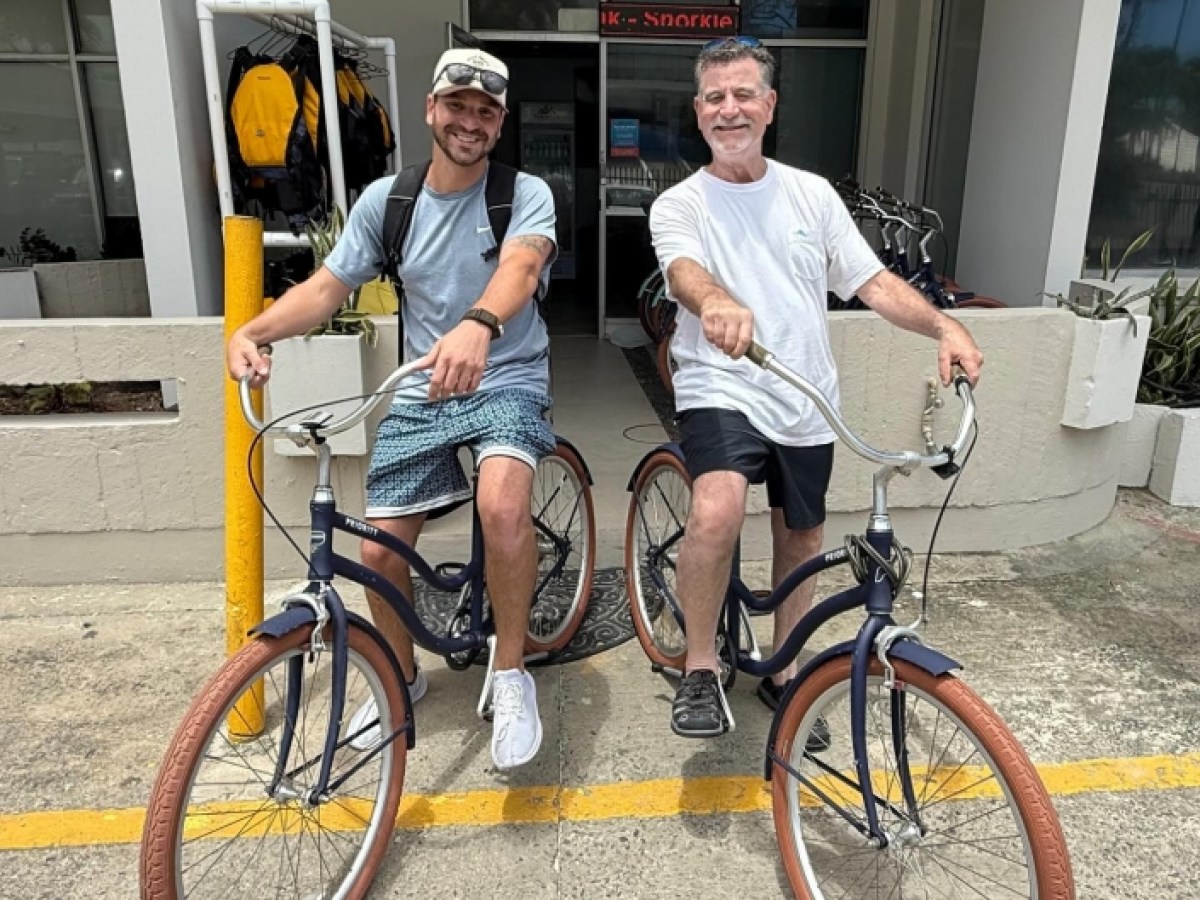 Two men pose with bikes outside a building, smiling at the camera.