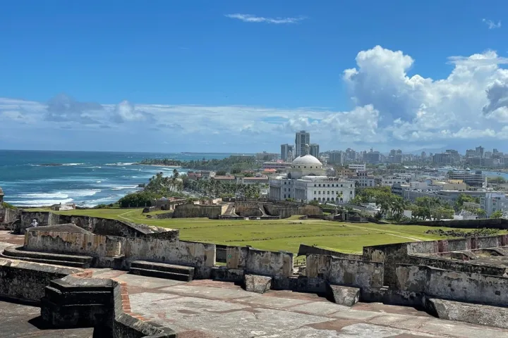 Historic fortress with ocean view, city skyline, and blue sky.
