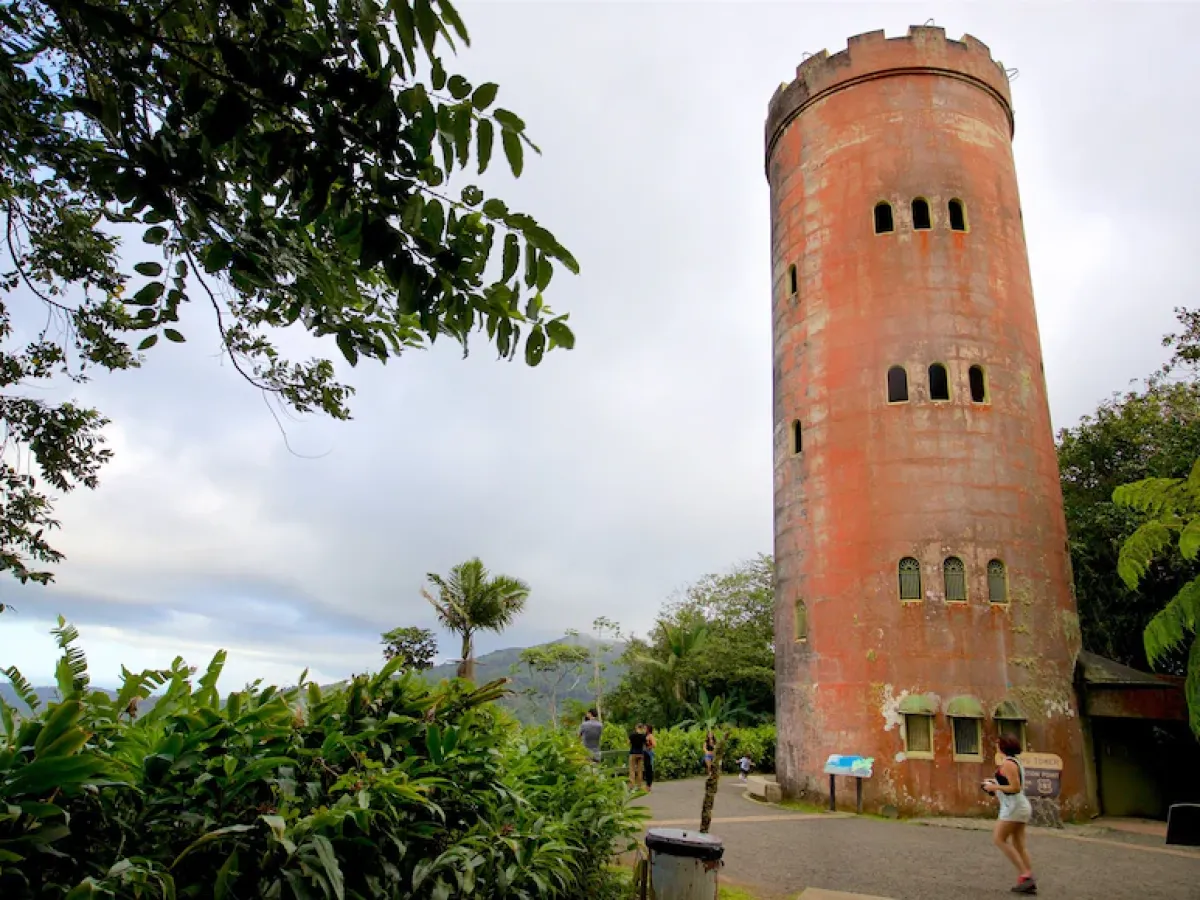 Tall round stone tower surrounded by lush greenery under a cloudy sky.