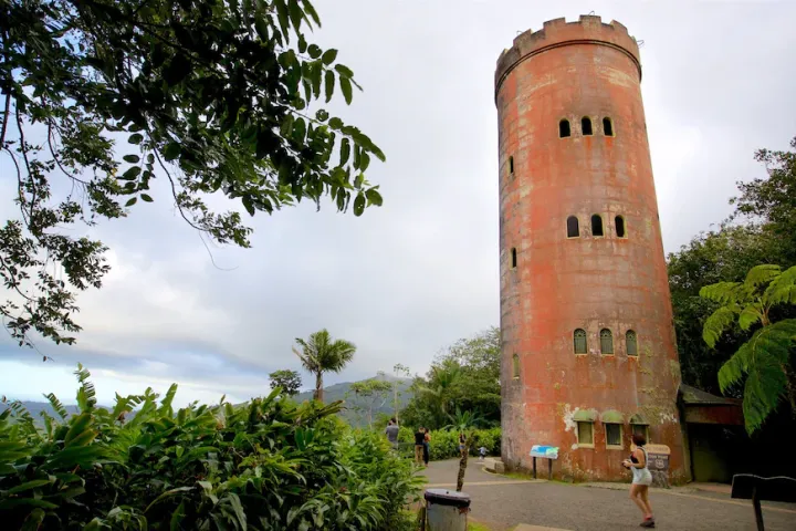 Tall round stone tower surrounded by lush greenery under a cloudy sky.