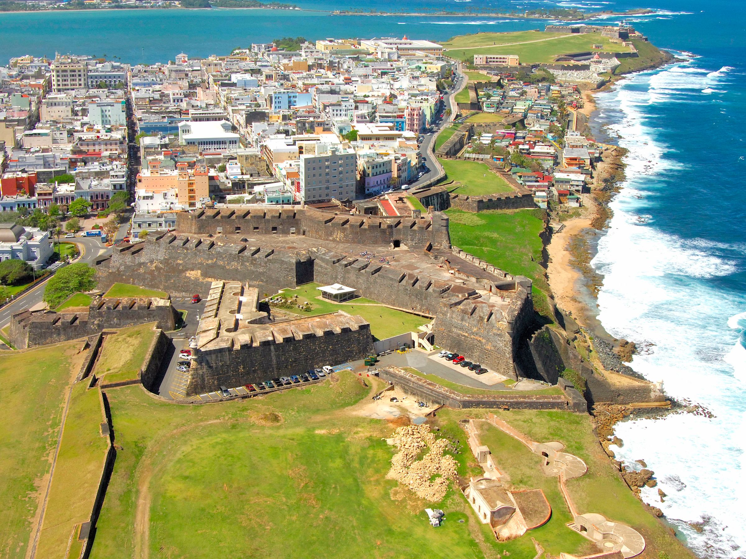 Aerial view of a coastal city with a historic fort and ocean waves.