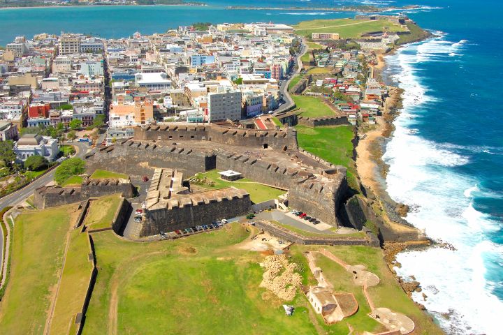 Aerial view of a coastal city with a historic fort and ocean waves.