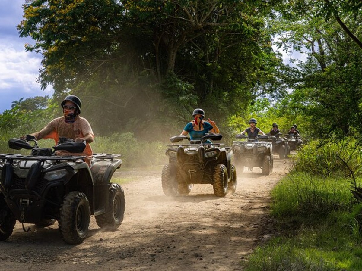 Group of people riding ATVs on a dirt trail in a forested area.
