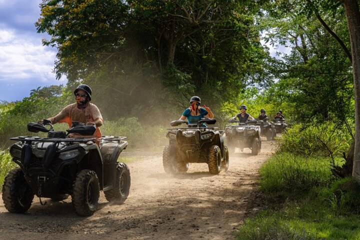 Group of people riding ATVs on a dirt trail in a forested area.