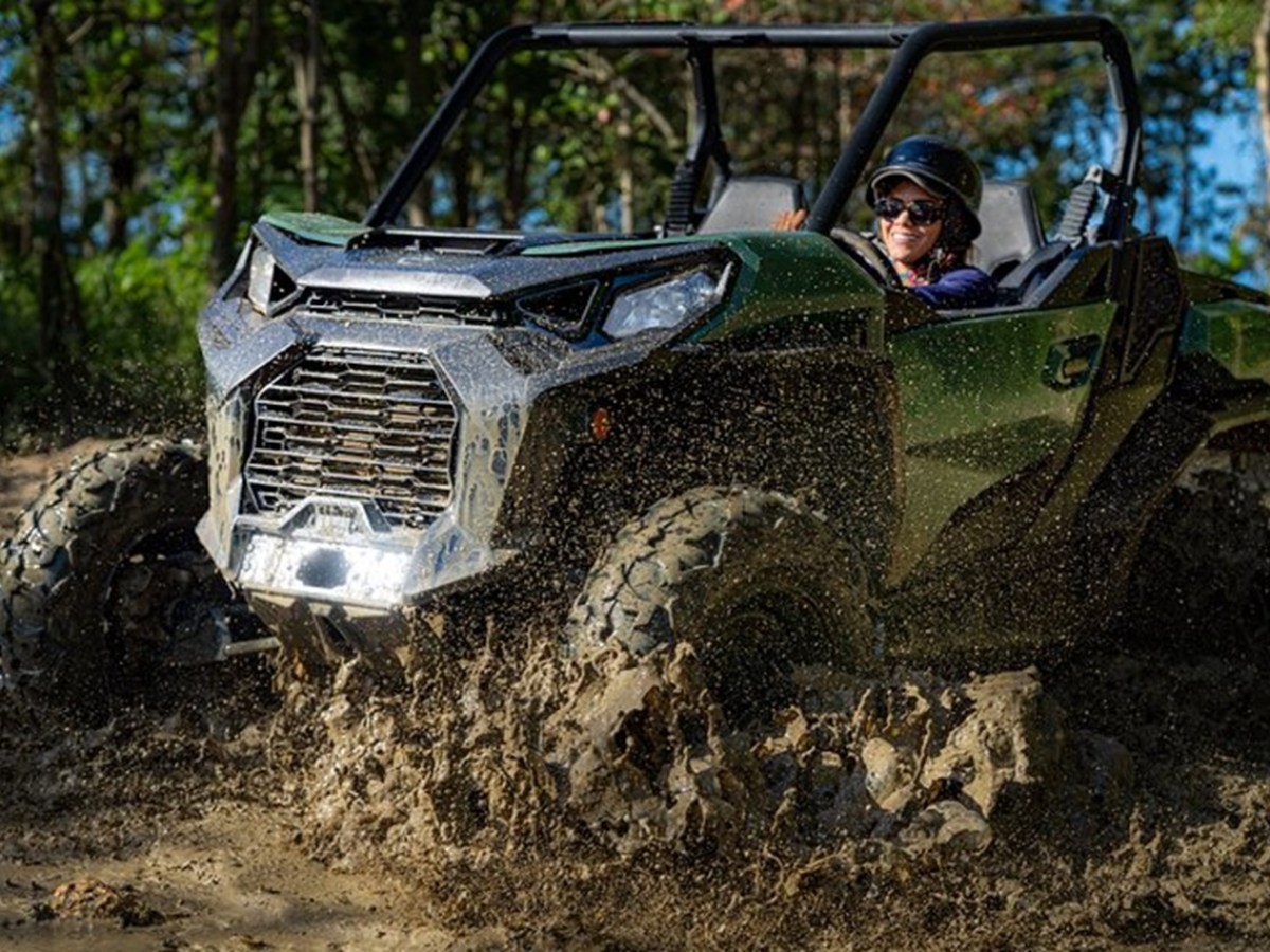 Person driving a green ATV through muddy terrain in a forest setting.