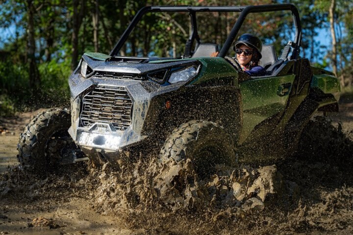 Person driving a green ATV through muddy terrain in a forest setting.