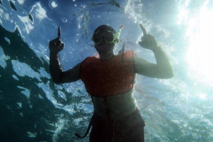 Underwater view of a person snorkeling with a life vest and mask, pointing upwards.