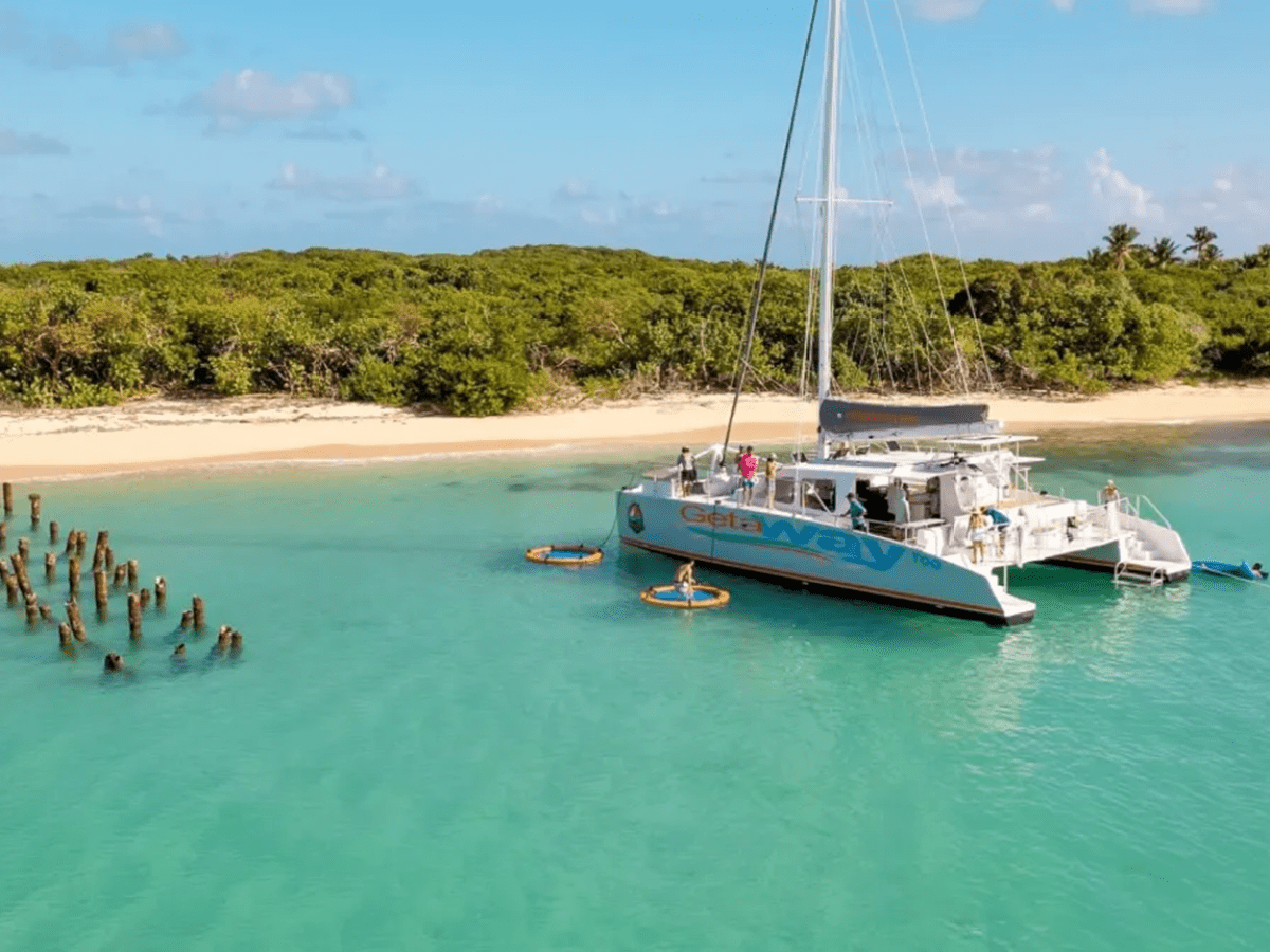 Catamaran anchored near a sandy beach with clear turquoise water and wooden posts.
