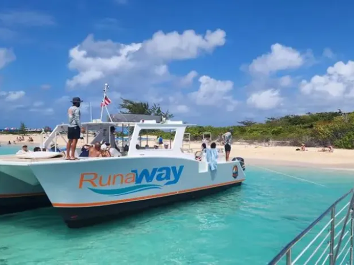Boat named 'Runaway' by a sandy beach with people and clear blue water under a partly cloudy sky.