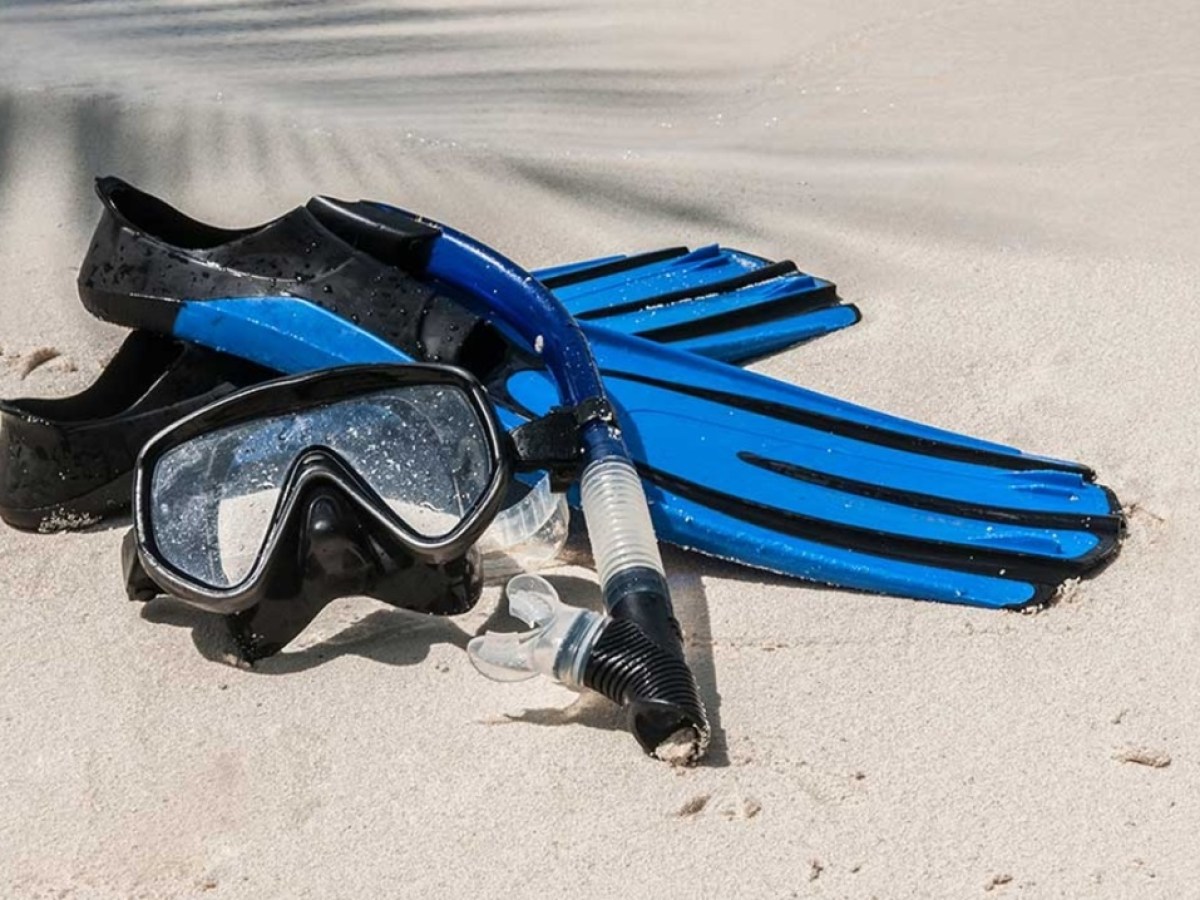 Snorkel gear with fins, mask, and snorkel tube on sandy beach.