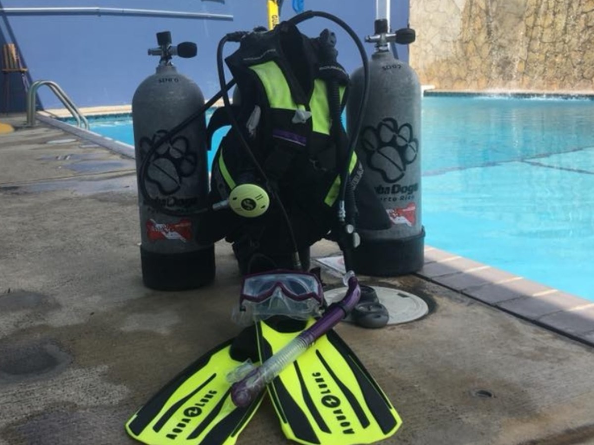 Diving equipment including fins, snorkel, mask, and tanks by a pool.