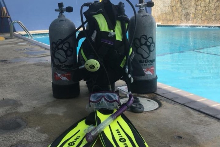 Diving equipment including fins, snorkel, mask, and tanks by a pool.