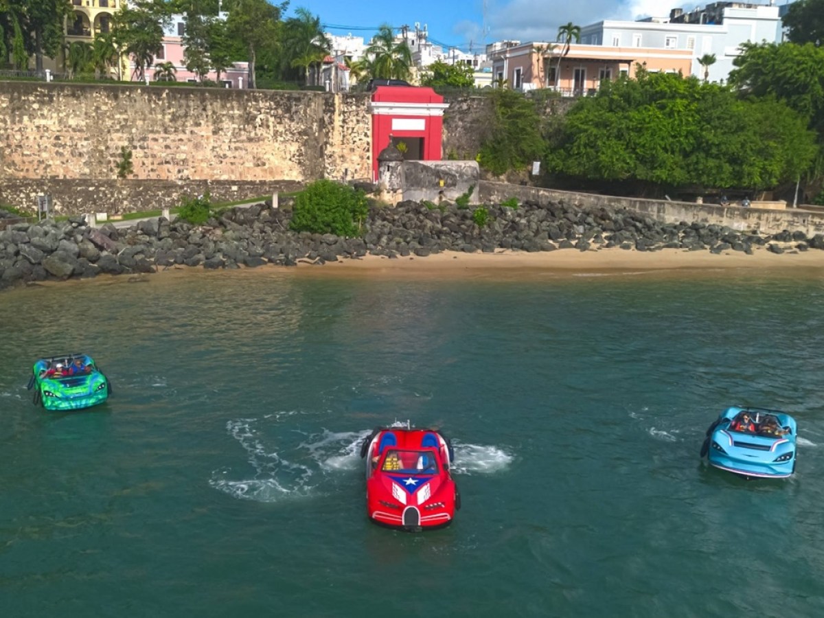 Three colorful boat cars on water near a historic stone fort and small beach.