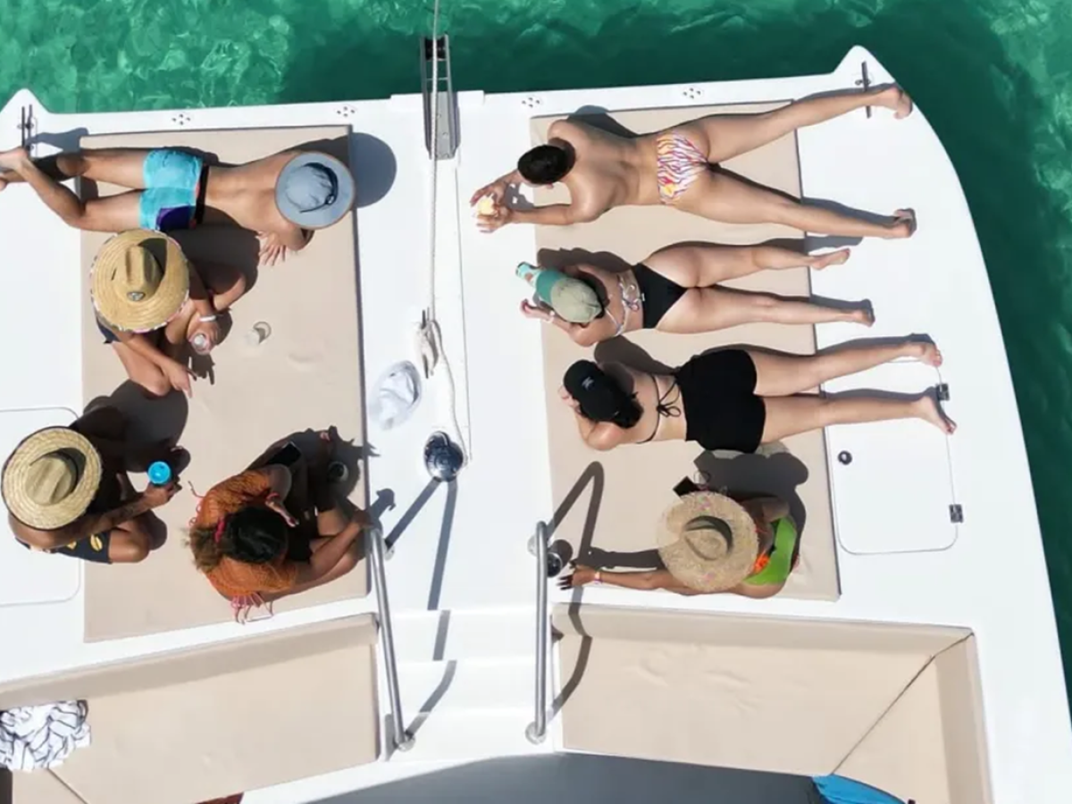 People sunbathing on a boat deck in swimwear, surrounded by clear blue water.