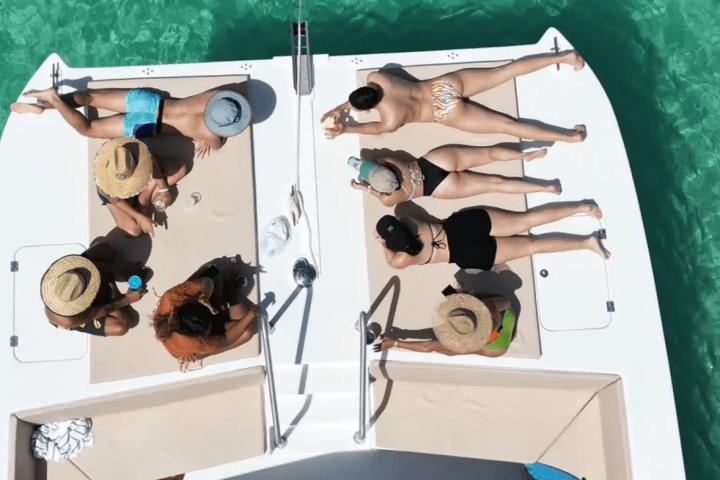 People sunbathing on a boat deck in swimwear, surrounded by clear blue water.