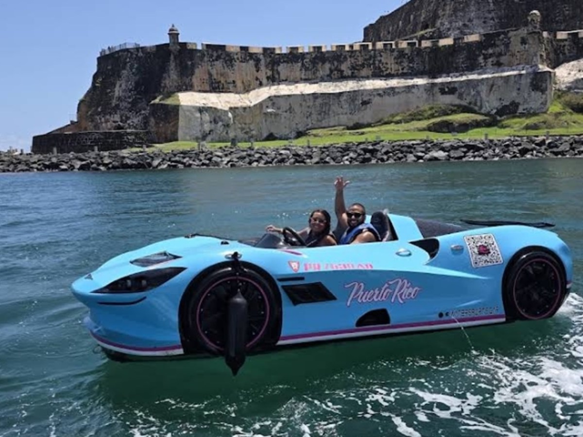 Two people in a blue car-shaped boat on water by a historic fort.
