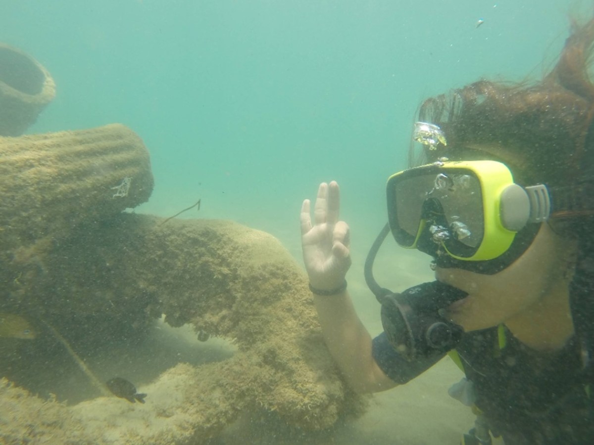 Scuba diver underwater near a coral structure, making an OK hand gesture.