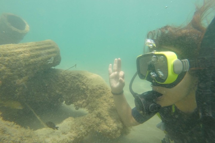 Scuba diver underwater near a coral structure, making an OK hand gesture.