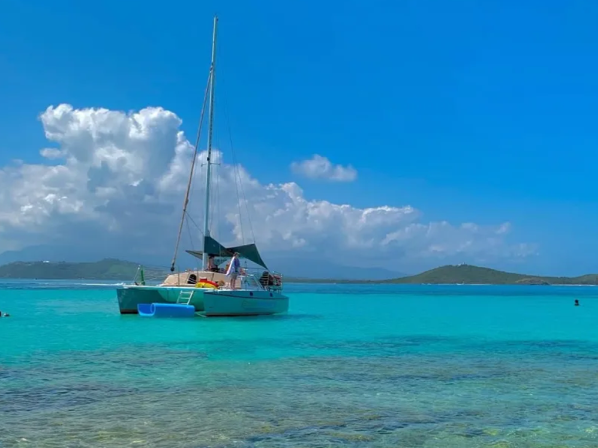 Sailboat anchored in turquoise sea with distant hills under a bright blue sky with clouds.