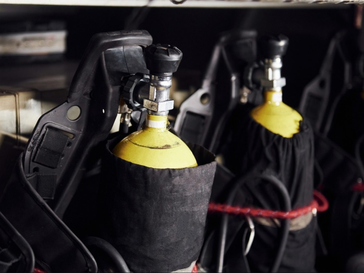 Row of yellow oxygen tanks with black covers and handles.