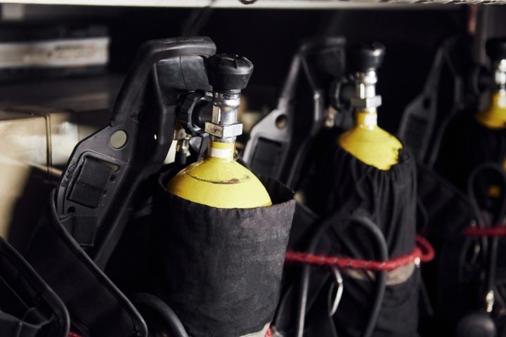 Row of yellow oxygen tanks with black covers and handles.