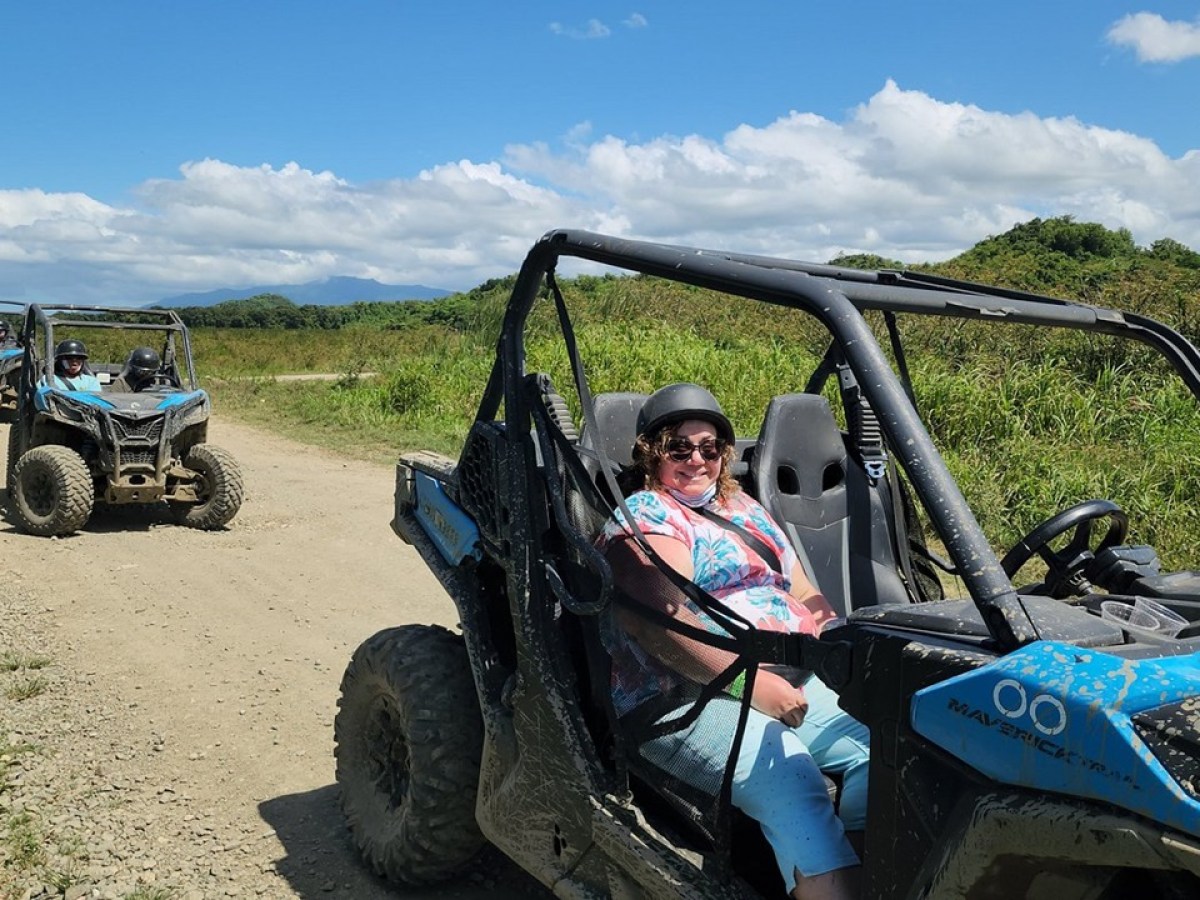 People driving off-road vehicles on a dirt path in a grassy landscape under a blue sky.